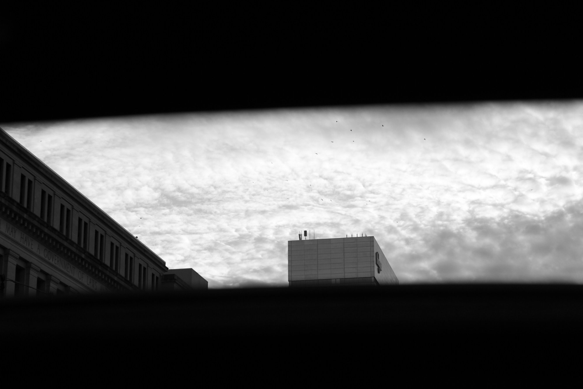 Black and white photo of clouds and downtown Cincinnati buildings, shot through a car moonroof