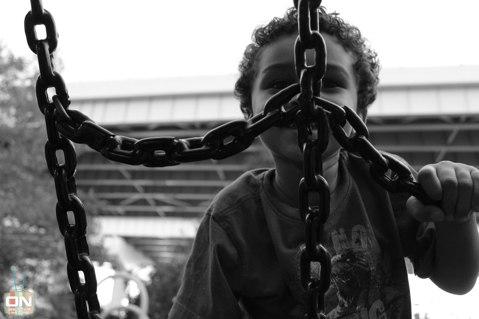 Black and white photo of a child looking through playground swing chains